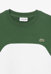Sudadera de cuello redondo verde y blanca, mezcla de algodón, que presenta un diseño de bloques de color contrastantes y un pequeño logotipo bordado de cocodrilo.