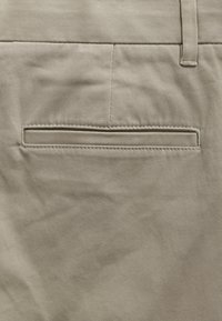 Beige szövet rövidnadrág, hátul egy keskeny, vízszintes nyílással rendelkező zsebbel és tiszta varrási részletekkel. Simító, laza stílus.