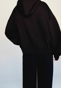 Czarna, oversize bluza z kapturem, z szerokimi rękawami i ściągaczami przy rękawach, zestawiona z czarnymi spodniami w stylu wide-leg. Gładka tekstura i luźny krój.