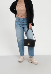 Černá texturovaná kabelka se zlatým kováním, nošená s béžovou košilí, černým sako a světle modrými džíny s vysokým pasem. Světlé tenisky dokončují outfit.