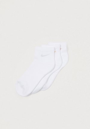 Tres pares de calcetines blancos tobilleros con pequeños logotipos de Nike en color plateado, amarillo y rojo sobre un fondo blanco.