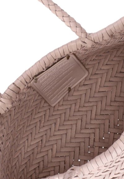 Intérieur d'un sac fourre-tout tressé rose clair montrant des poignées tressées et une étiquette rectangulaire cousue à l'intérieur près du bord.