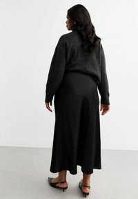 Jupe noire, longueur cheville avec une texture lisse, assortie à un pull oversize noir. Des ballerines noires pointues complètent le look.