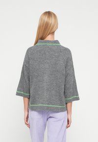 Hall hallitatud kampsun kraega, mis on roheliste õmblusdetailidega ja laiade küünarnukipikkuste varrukatega. Kandmiseks koos helelilla soonikuga pükstega.