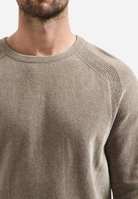 Lichtbruin gebreid truitje met een ronde hals, ribbelstructuur en subtiele details op de schoudernaden. De stof lijkt zacht en comfortabel.