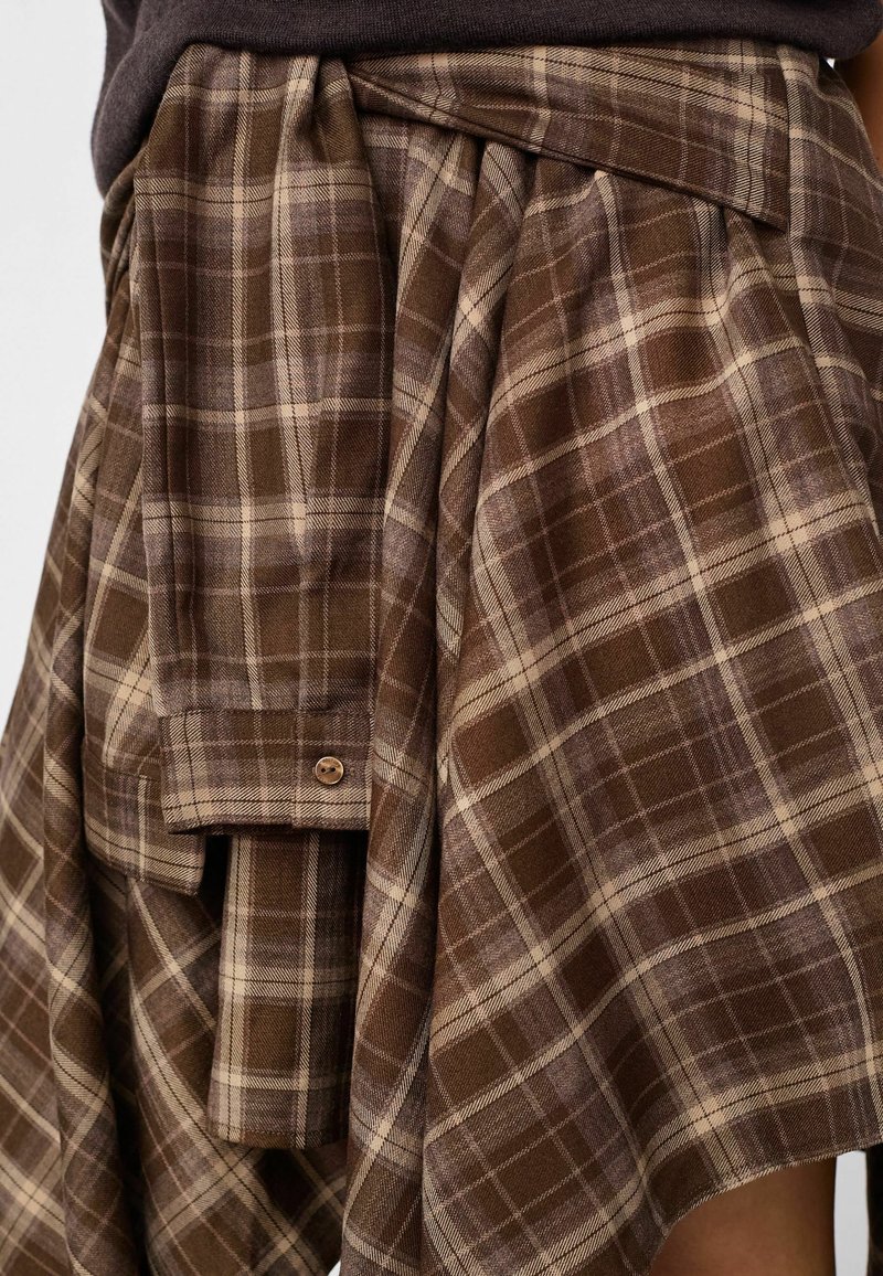 Ceinture en tissu à carreaux marron et beige nouée autour de la taille sur une jupe plissée assortie avec un détail bouton.
