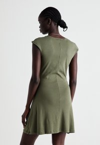 Vestido verde-oliva feito de algodão macio, com mangas curtas, corte descontraído e barra godê, apresentando um detalhe de costura nas costas.