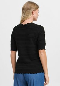 Top en tricot noir avec des rayures horizontales texturées, encolure et bords des manches à volants. Design ajusté. Vue arrière affichée.