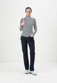 Tricou cu dungi, cu mânecă lungă și guler înalt, în alb și negru, asortat cu blugi de culoare bleu închis și cizme scurte de culoare deschisă. Include o geantă mică pentru umăr.