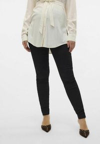 Svarte skinny jeans kombinert med en lang kremfarget bluse med knyteliv og mansjetterte ermer, båret med brune spisse hæler.