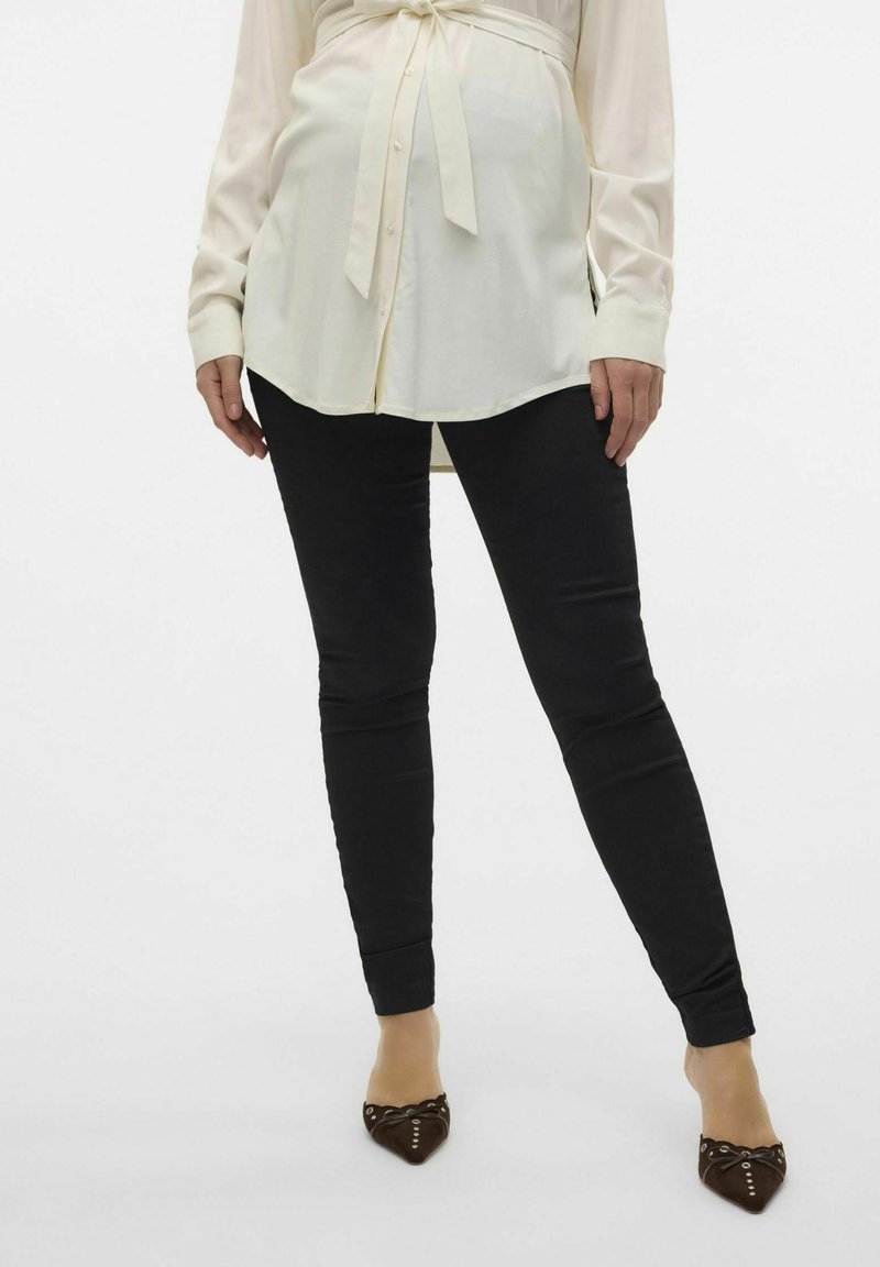 Czarne skinny jeans w połączeniu z długą jasnobeżową bluzką z wiązaniem w talii i mankietami, noszone z brązowymi czółenkami o spiczastym nosie.