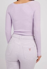 Lila prążkowana bluzka z długim rękawem w połączeniu z jasnofioletowymi dżinsami. Dżinsy mają dwie tylne kieszenie z czerwoną trójkątną naszywką.