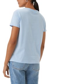 Lichtblauwe katoenen t-shirt met een ronde hals en korte mouwen, met een ontspannen pasvorm en rechte zoom. Draagt met blauwe jeans.