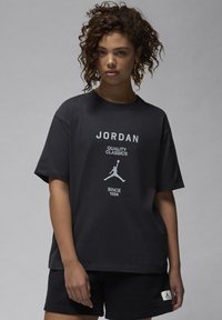 Black cotton t-shirt featuring white "JORDAN" text and a graphic logo of a jumping man. Short sleeves and relaxed fit. Paired with black shorts.
