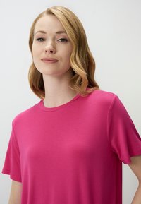 Fuchsia T-shirt met korte mouwen en ronde hals. Gemaakt van gladde stof, met een ontspannen pasvorm en minimale naden. Eenvoudig ontwerp.
