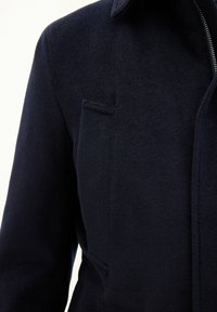 Merinovillakangastakki, jossa on tekstuuri, esittelee terävää kaulusta ja yksittäistä rintataskua. Vetoketjusuljin ja muotoiltu istuvuus.