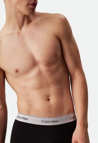Black boxer briefs with a grey waistband featuring the "Calvin Klein" logo in black. The material appears soft and fitted.