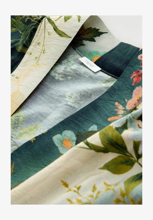 Floral patterned fabric showcasing vibrant flowers and leaves in shades of green, beige, and peach, with a visible brand label.