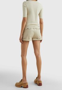 Beige short-sleeve top and khaki shorts. The shorts feature rolled hems and back pockets. Model wears chunky tan sandals with a brown accent.