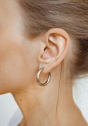 Silberne Creolen mit einer glatten, glänzenden Oberfläche, in runder Form gestaltet und mit einem kleinen Akzent am Verschluss, getragen am Ohr eines Models.