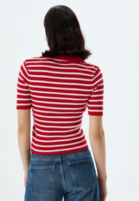 Haut en tricot rayé rouge et blanc, à côtes, avec un col court et des manches courtes, associé à un jean en denim bleu avec des poches arrières.