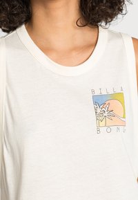 Top sin mangas de algodón crema con un estampado gráfico de palmeras y un atardecer, con el texto "BILLA BONG" en negro. Textura suave.