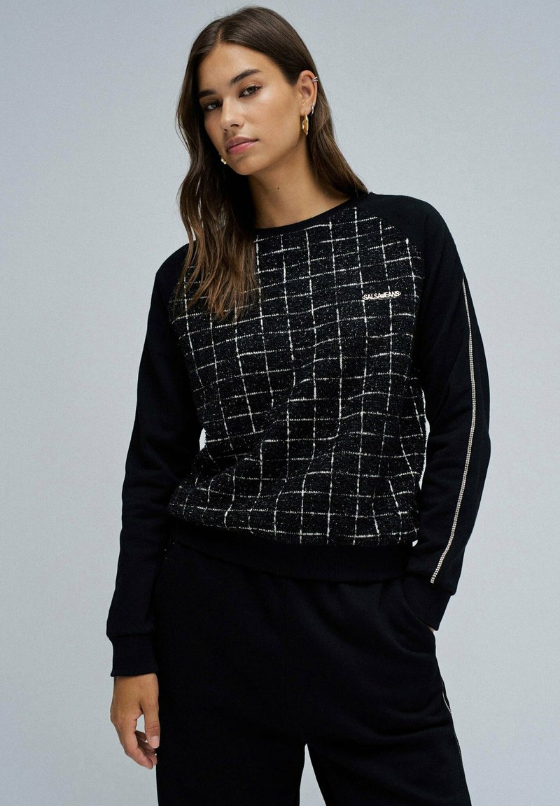 Sweatshirt noir avec un motif de grille texturé, présentant des manches noires contrastantes et des accents métalliques sur le côté.