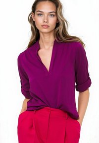 Fuksjowa bluzka z częściowym kołnierzykiem, zapiętymi rękawami podwiniętymi, w zestawieniu z jasnoróżowymi spodniami z wysokim stanem; gładka faktura.