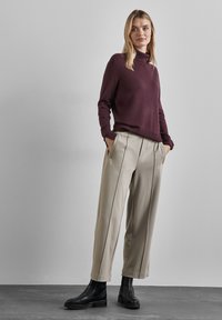 Un pull à col roulé bordeaux, un pantalon large crème avec des coutures verticales et des bottines noires. Textures lisses et coupe moderne décontractée.