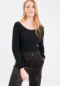 Maglietta nera a maniche lunghe con scollo ampio e maniche nere testurizzate, abbinata a pantaloni in velluto a coste scuri con vita elastica.