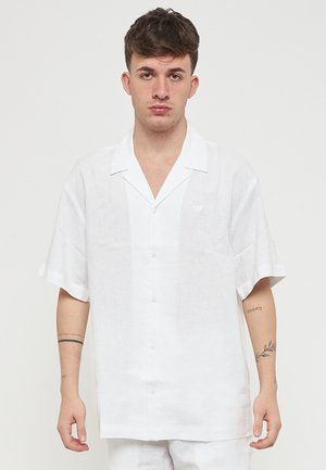 Camicia bianca in lino a maniche corte con colletto, dotata di bottoni frontali e di un piccolo logo sul petto. Tessuto liscio e vestibilità comoda.