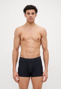 Bóxer negro con un diseño ajustado, fabricado en material elástico. Presenta una cinturilla ancha con la palabra "ARMOUR" en letras grises.