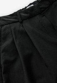 Pantaloni in tessuto plissettato nero con una texture liscia, dotati di una vita aderente e dettagli di cucitura orizzontale nella parte superiore.