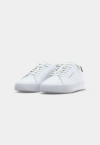 Ein Paar weiße Low-Top-Sneaker mit Schnürsenkeln und dezentem "Tommy Hilfiger"-Branding an der Seite und auf der Zunge vor einem schlichten Hintergrund.