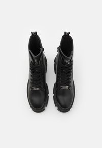 Botas de tobillo de cuero negro con cuello acolchado, diseño con cordones, acentos metálicos y suela de goma gruesa. Cierre de cremallera en el lateral.