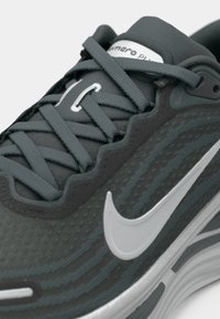 Nærbilde av mørkegrå Nike joggesko med lys grå swoosh-logo og tykk, polstret såle.