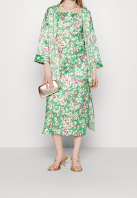 Sukienka w kwiaty i dopasowany kimono w zielonym kolorze, z różowymi i białymi kwiatami, złotą kopertówką i sandałami na cienkim obcasie. Gładki materiał, długość do kolan.