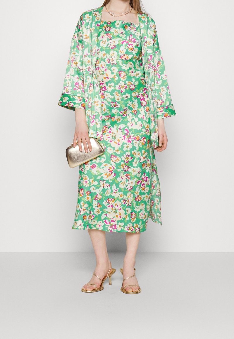 Sukienka w kwiaty i dopasowany kimono w zielonym kolorze, z różowymi i białymi kwiatami, złotą kopertówką i sandałami na cienkim obcasie. Gładki materiał, długość do kolan.