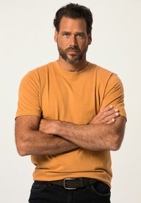 Sennepsgul kortærmet t-shirt lavet af bomuld, med rund hals og normal pasform, båret med mørke jeans og et brunt bælte.
