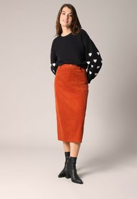 Zwarte trui met witte hartpatronen op de mouwen, gecombineerd met een oranje corduroy midi-skirt en zwarte enkellaarsjes.
