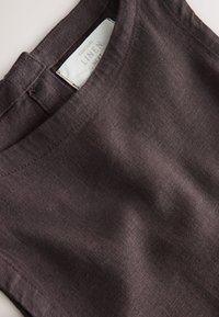Close-up of dark brown linen fabric dress with a round neckline and visible fabric label inside the collar.