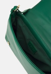 Zelená kožená kabelka s hladkým povrchem, vybavená zlatým hardwarovým zapínáním, a prostorným interiérem s textilní podšívkou a značkovou cedulkou.