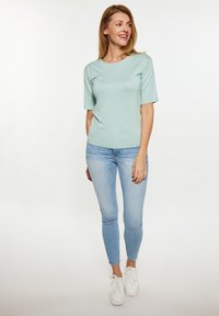Světle modrý pletený top s krátkými rukávy, kombinovaný se světle modrými slim džíny a bílými teniskami. Jednoduchý design s pohodlným střihem.