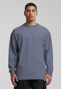 Long-sleeve striped shirt in navy and white cotton, featuring a crew neckline and relaxed fit. Sleeve ends have subtle logo detail.