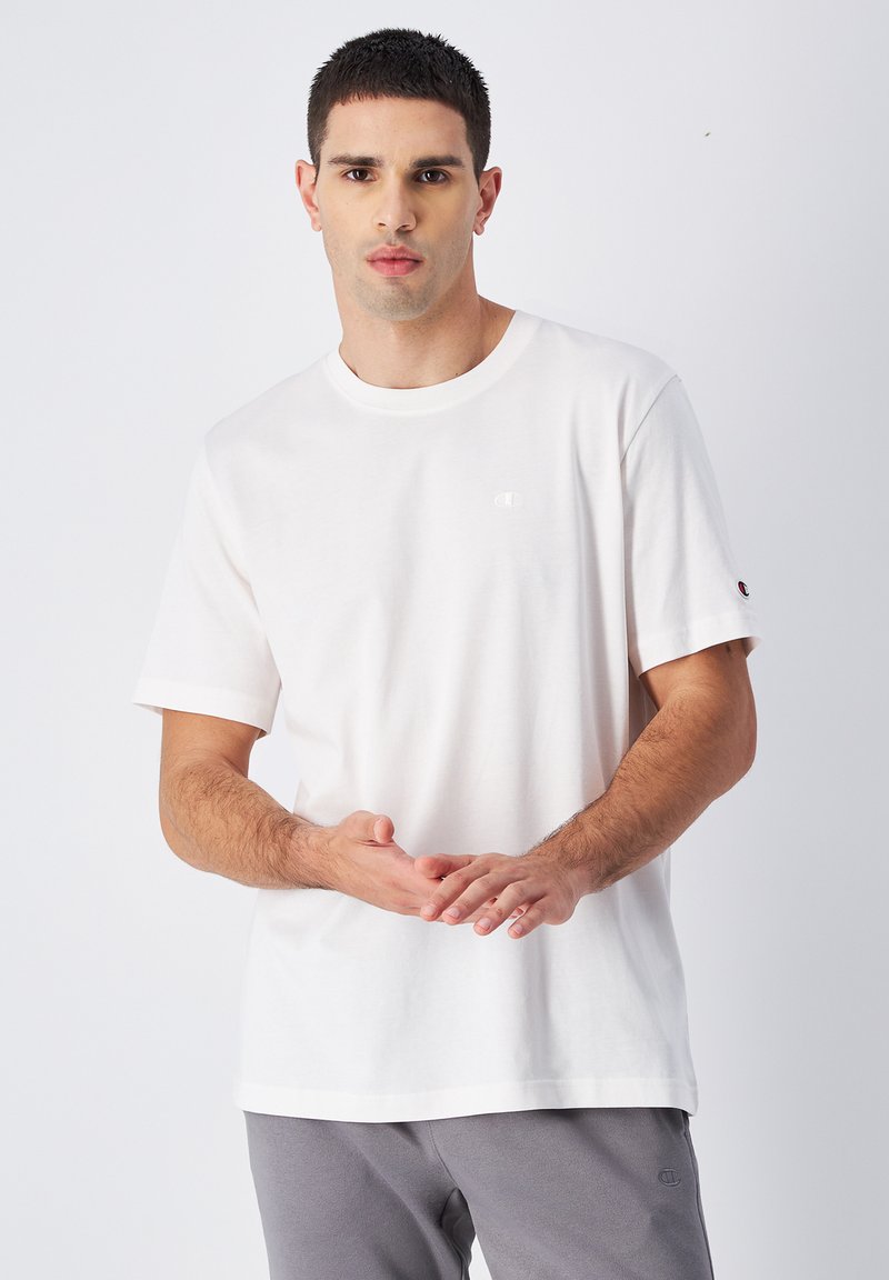 Weißes Baumwoll-T-Shirt mit Rundhalsausschnitt und kurzen Ärmeln, das ein kleines gesticktes Logo auf der Brust und einen Logo-Akzent auf dem Ärmel aufweist.