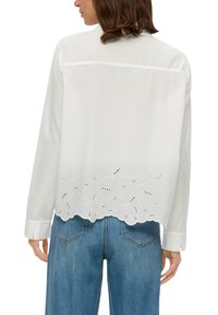 Weißes Baumwollhemd mit gesticktem Wellenrand, das florale Muster und Durchbrüche aufweist. Mit langen Ärmeln und einer lockeren Passform.