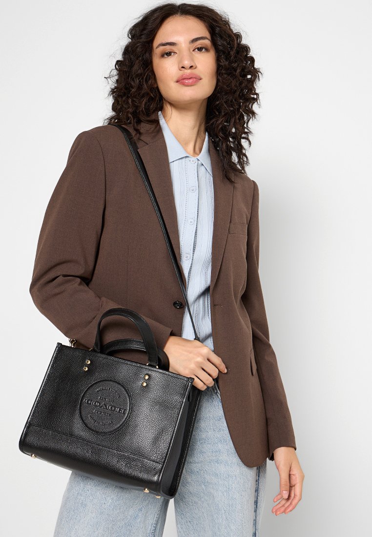 Bolso de mano de cuero negro texturizado con una forma estructurada, que presenta una chapa con el logo, asas cortas y detalles en hardware dorado.