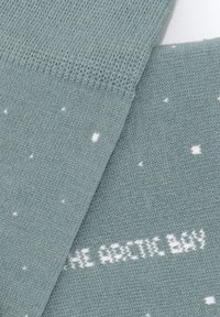 Calcetines azul verdoso claro con puntos blancos, con tejido de punto texturizado y una etiqueta que dice "THE ARCTIC BAY" en letras blancas.