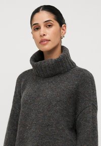 Maglione grigio realizzato in tessuto a maglia screziato, con un colletto alto e ripiegato e una vestibilità rilassata. Accentuato da sfumature multicolori diffuse.