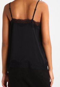 Camisole noir avec des accents en dentelle le long de l'encolure et de l'ourlet, dotée de bretelles fines réglables et d'une texture de tissu lisse et léger.